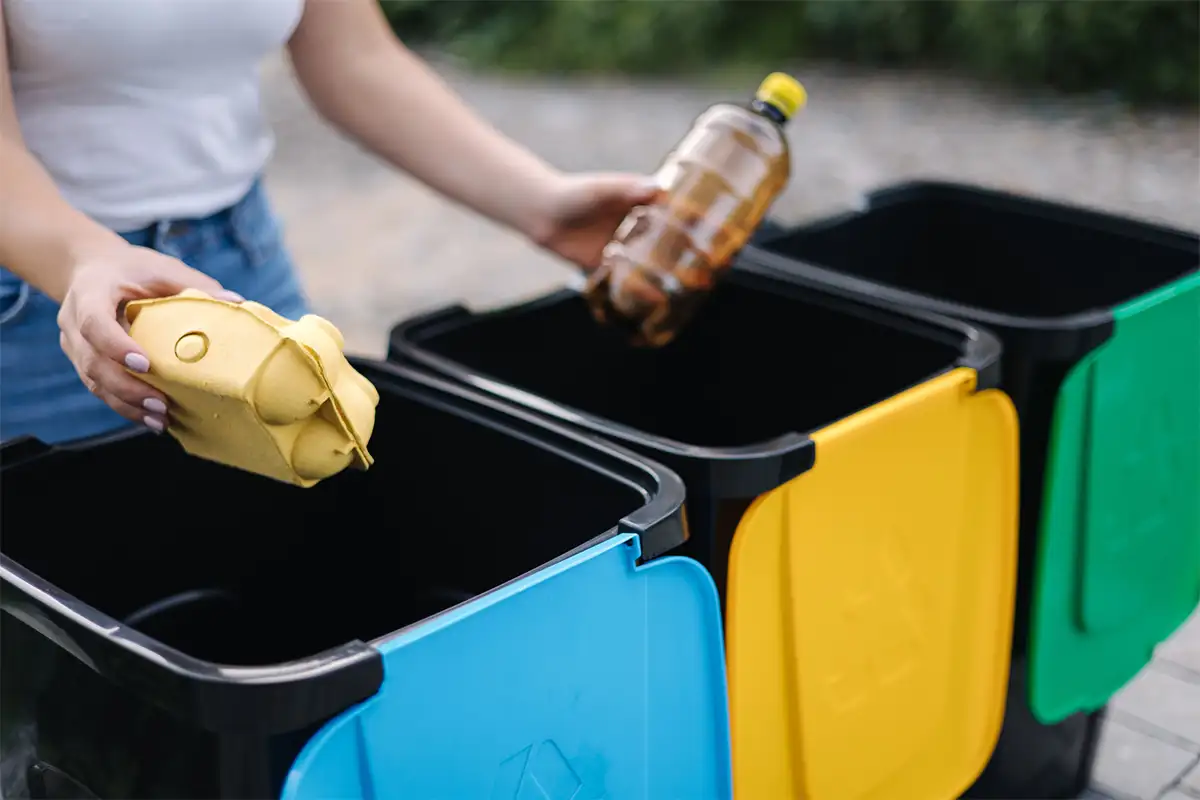 Mains d'une femme hésitant au dessus de poubelles de tri bleu, jaune et verte