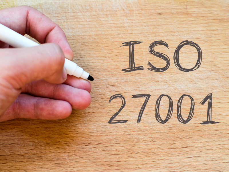 Gros plan d’une main qui écrit « ISO 27001 » au feutre sur une surface en bois