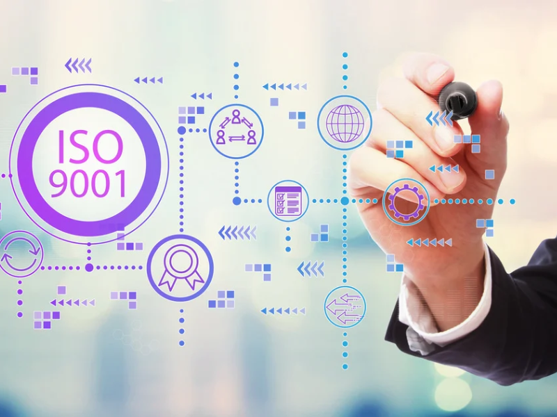 Gros plan d'une main tenant un feutre et pointant un tableau transparent sur lequel est écrit "ISO 9001".